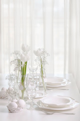 Happy Easter! Decor and table setting of the Easter table with white tulips and dishes of white color.