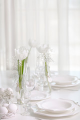 Happy Easter! Decor and table setting of the Easter table with white tulips and dishes of white color.