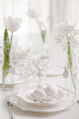 Happy Easter! Decor and table setting of the Easter table with white tulips and dishes of white color.