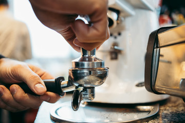 Close up shot of professional bartender preparing espresso coffee in exclusive cafe bar or cafeteria. He using coffee mill or grinder.