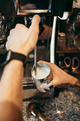 Close up shot of experienced barman or bartender hands preparing milk for delicious and fresh espresso coffee drink on machine.
