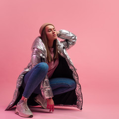 Stylish fashionable and modern young woman in a puffy light down jacket. The jacket is a silver...