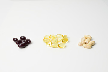 Three bunches of multivitamins, fish oil and astaxanthin. Polyunsaturated fatty acids in the middle. White background. Close-up.