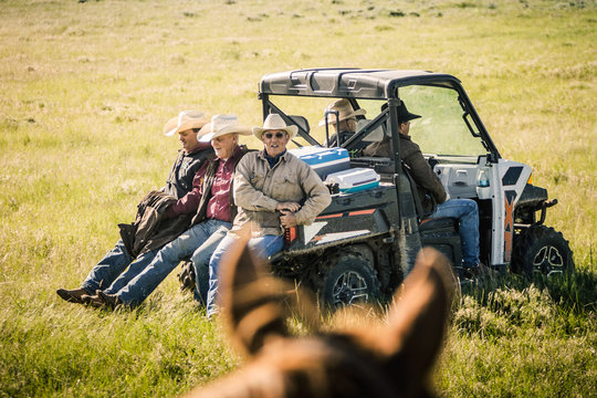 Cowboys riding across field on the back of an ATV. Cody, Wyoming, USA