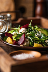 Fresh arugula salad with mozzarella, avocado, beetroot, walnuts and oranges. Espresso and orange juice dressing. Served on wooden tray. 