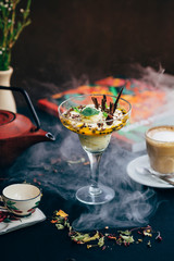 desert on a cocktail glass with coffee, tea pot and tea cup with a book and smoke