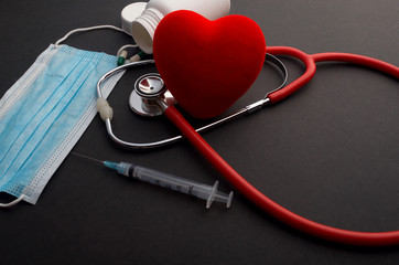 Face mask, red heart and stethoscope on dark background. 