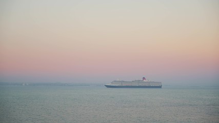 Gimbal shot of a cruise ship on background of pink sunset and horizon. Cruise ship liner goes on the pink horizon sunset line on the blue sea, tourist cruise liner