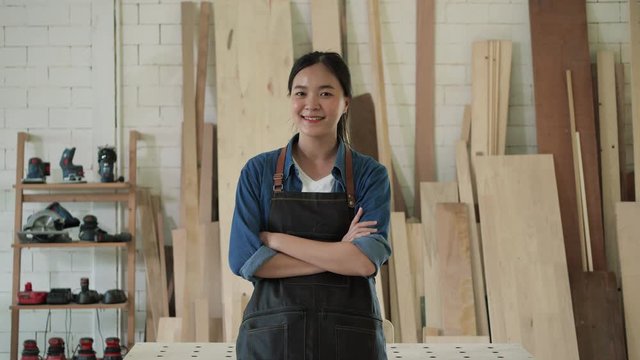 Asian chinese woman carpenter standing and smiling in home workshop. Teenage female is high experience and skill professional in lumber furniture. concept of sme, business and handmade industry.