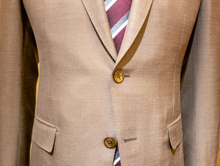 Beige mens suit with red striped tie close up, one button undone