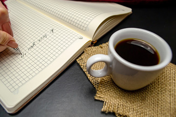 Ballpoint pen writes I love you in a notebook near a cup of coffee on a black background