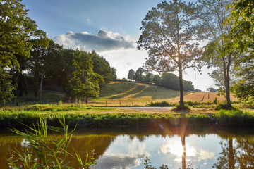 Image of a rural meadow with low sun, trees and canal