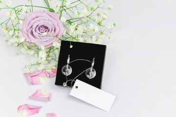 Luxury elegant stylish earrings with natural rock-crystal on a velvet black pillow with flowers roses and petals, mockup. Beauty Accessory Brand Concept