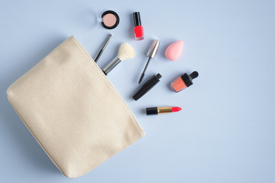 Make-up cosmetic bag on blue background. Stylish makeup artist pouch with beauty products. Flat lay, top view