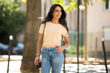 beautiful young smiling hispanic woman in city with purse