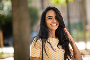 Close up happy young arabic woman smiling with hand in hair outside