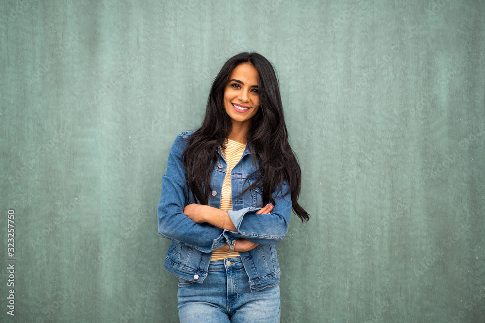 Wall mural attractive young latin woman smiling by green wall with arms crossed