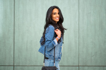 smiling young latin woman with handbag by green wall