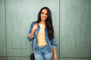 beautiful young arab woman with purse smiling by green wall