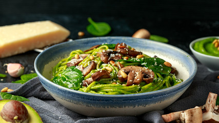 Vegan garlic mushroom pasta with spinach and avocado pesto drizzled with sesame seeds and roasted pine nuts