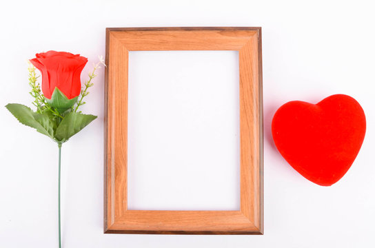 Flat lay view of artificial red roses with heart shape and wooden frame on white background. Love and Valentine's Day concept.