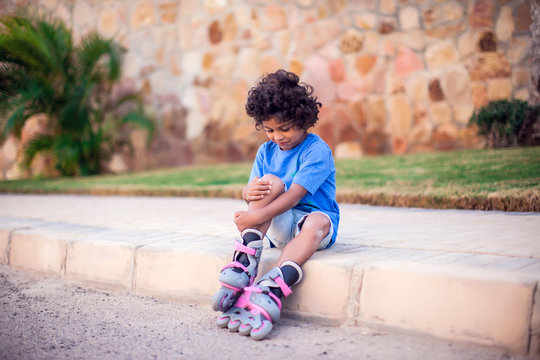 A Kid Boy On Rollerskates Fell Down And Feels Pain. Children, Activity And Healthcare Concept