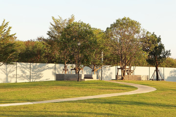Outdoor public park with beautiful slope contour lawn and big trees on warm and lovely day in sunset summer tropical season.