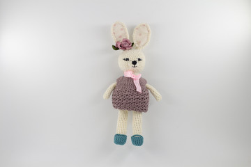 knitted toy rabbit in a sweater-dress with a flower on the ear on a white background