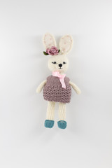 knitted toy rabbit in a sweater-dress with a flower on the ear on a white background