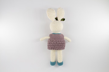 knitted toy rabbit in a sweater-dress with a flower on the ear on a white background