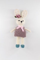 knitted toy rabbit in a sweater-dress with a flower on the ear on a white background