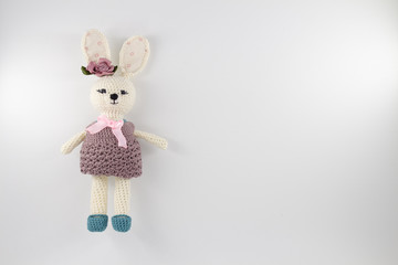 knitted toy rabbit in a sweater-dress with a flower on the ear on a white background