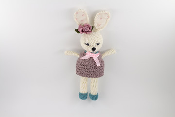knitted toy rabbit in a sweater-dress with a flower on the ear on a white background