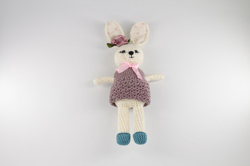 knitted toy rabbit in a sweater-dress with a flower on the ear on a white background