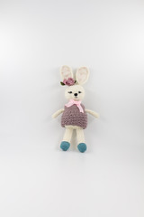 knitted toy rabbit in a sweater-dress with a flower on the ear on a white background