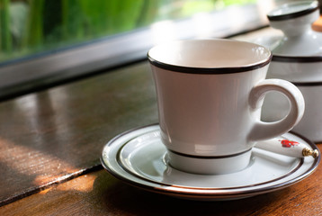 White ceramic coffee cup on the plate is placed on the wooden table in coffee cafe