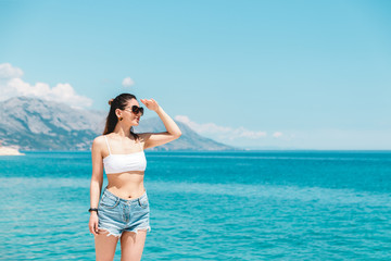 Fototapeta na wymiar time to travel. beautiful woman in white topic and jeans shorts alone on seaside looking to the blue ocean and enjoying the view