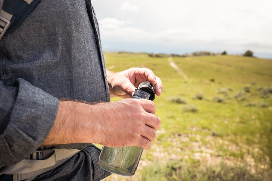 Close-up of man holding a water bottle while hiking in rural prairie landscape. Cody, Wyoming, USA