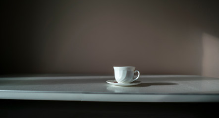 abstract white cup with hot drink in the plate placed on white table in the morning, hard sun and shadows