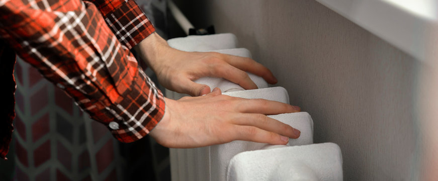 Frozen Hands Touch A Heating Battery At Home During Winter Season