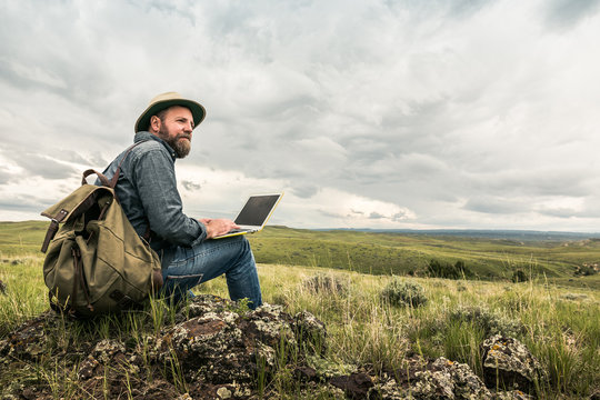 Bearded man working on laptop in rural prairie landscape. Cody, Wyoming, USA