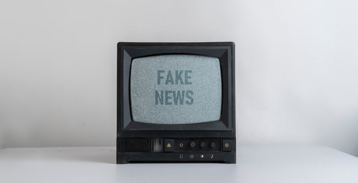 the old vintage tv with gray noise on screen with fake news text overlay, standing on shelf at home