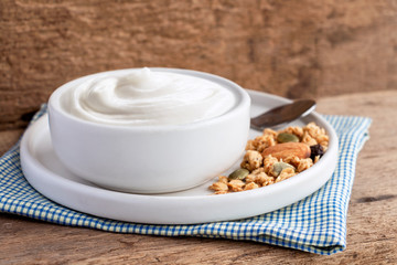 Healthy flavored yogurt in ceramic bowl with cereal and granola on cloth with wood background with copy space for your text.