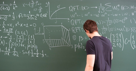 male person writing text with piece of chalk on blackboard, doing maths and physics equations