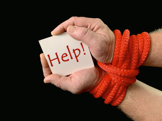 Hands tied with a rope, on a black background. Tied hands are holding a note with the inscription....