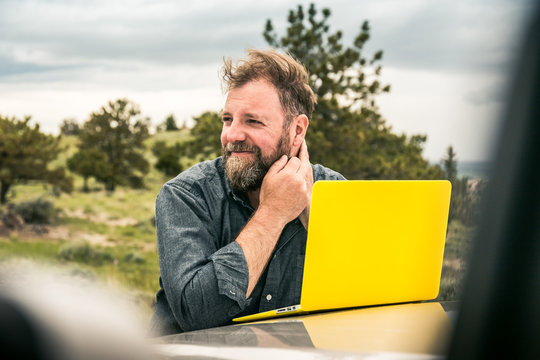 Bearded man with laptop on truck observing rural prairie setting. Cody, Wyoming, USA