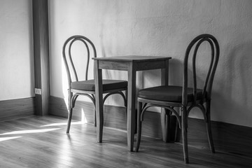 The small table and chairs in the small room next to the window and natural light from the outside , black and white style. 