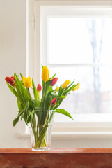 red and yellow tulips in vase on the windowsill bright, country style, in sunlight, bouquet for Easter decoration against an open background with copy space.