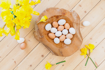Obraz na płótnie Canvas easter background decoration with eggs in wooden bowl, green leaves and Easter bells, daffodil flowers on wooden floor. Spring decoration. Naturally designing sustainable