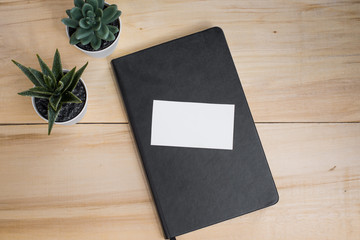 Diary, white business card mockup and plants on a wooden table. Workplace. Business. Freelance